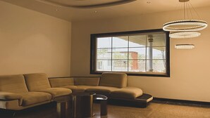 A modern living room with a beige sectional sofa, a round coffee table, and a large window with a view of buildings outside.