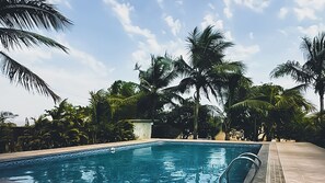 A swimming pool surrounded by palm trees and a clear sky. - Discover Resorts Pali (Sudhagad)