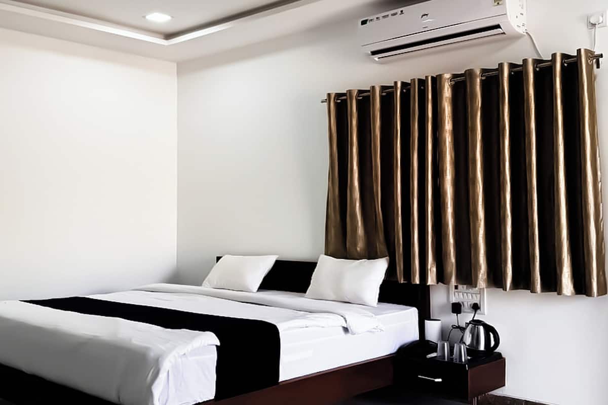 Una camera d'hotel con un letto, un comodino, un condizionatore d'aria e una tenda.