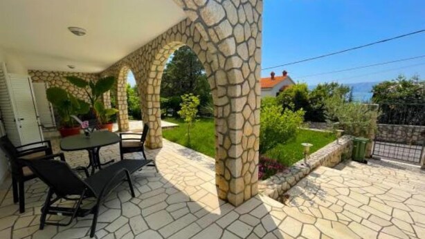 Une terrasse couverte avec des piliers en pierre, une table et des chaises.