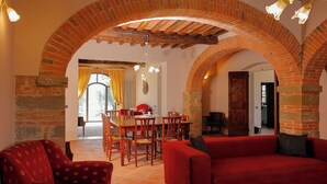 Un comedor con un arco de ladrillo, muebles tapizados en rojo y una araña.