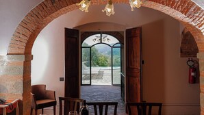 Un comedor con una mesa de madera, sillas y una botella de vino. Se aprecia una pared de ladrillo en arco y un techo de madera.