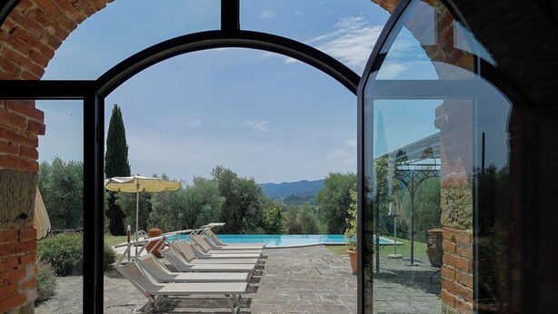 Vista a través de un ventanal de un área de piscina con sillas de descanso y un cielo despejado.