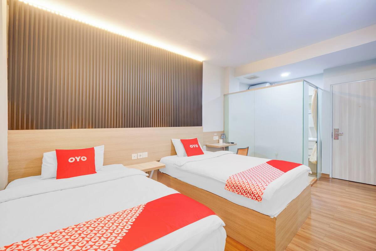 A hotel room with two beds, each with a red and white patterned bedspread, a wooden headboard, and a wall-mounted light fixture.