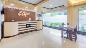 A hotel reception area with a wooden reception desk, a glass table, and chairs. - Hotel O Tanjung Duren Near Mall Citraland Formerly Suba Hotel (Jakarta)