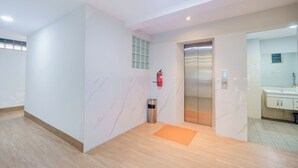 A clean, modern lobby with a wooden floor, a marble wall, a fire extinguisher, an elevator, and a bathroom with a sink and cabinets. - Hotel O Tanjung Duren Near Mall Citraland Formerly Suba Hotel (Jakarta)