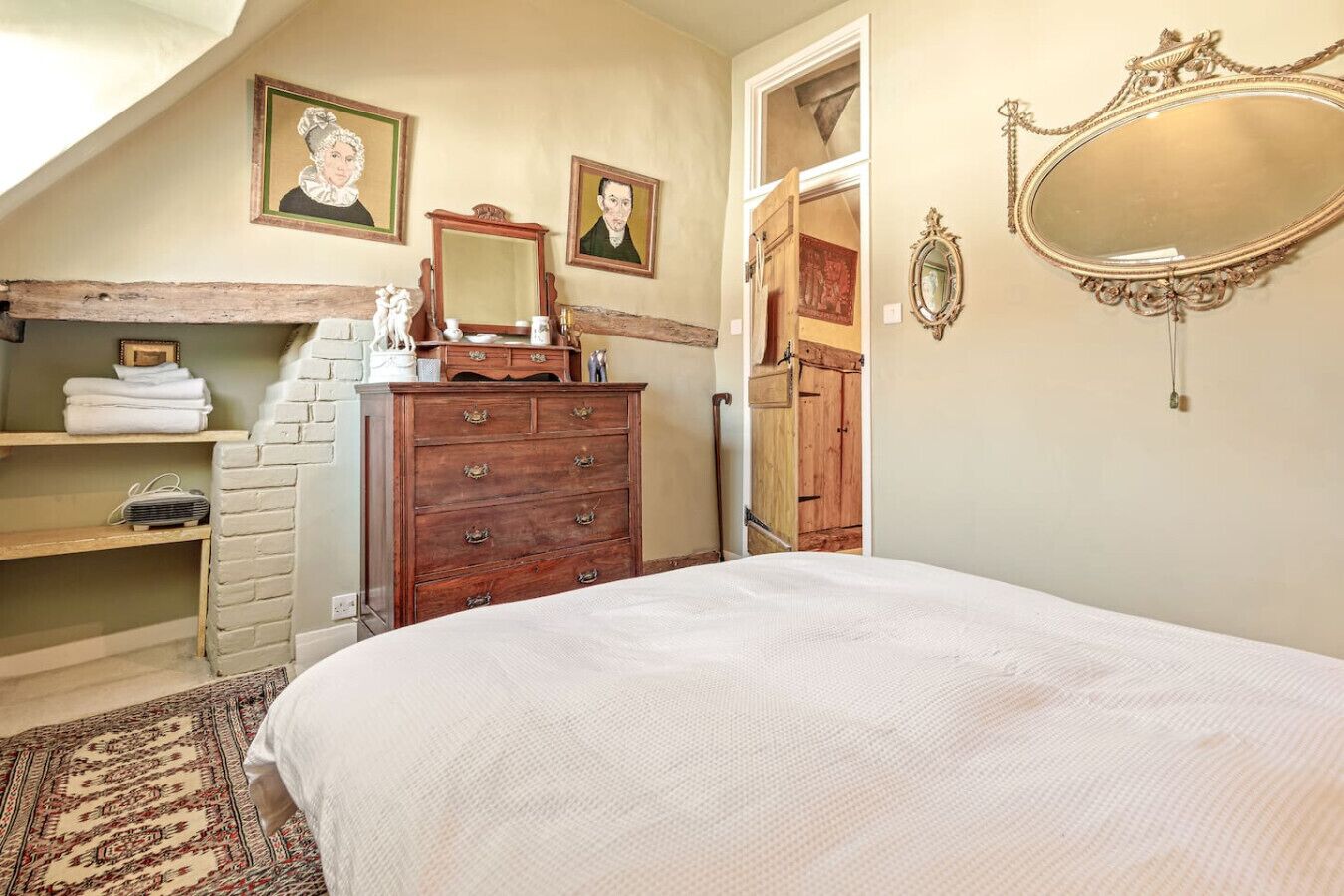 A bedroom with a bed, wooden dresser, and two framed portraits on the wall.