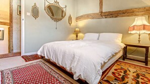A bedroom with a large bed, two wall-mounted mirrors, a wooden beam ceiling, and a patterned rug. - Basketmakers Cottage (Henley-On-Thames)