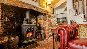 A cozy room with a stone fireplace, a red leather sofa, and a staircase. - Basketmakers Cottage (Henley-On-Thames)