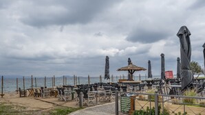 Un restaurante frente al mar con terraza, una sombrilla de paja y vistas al océano.