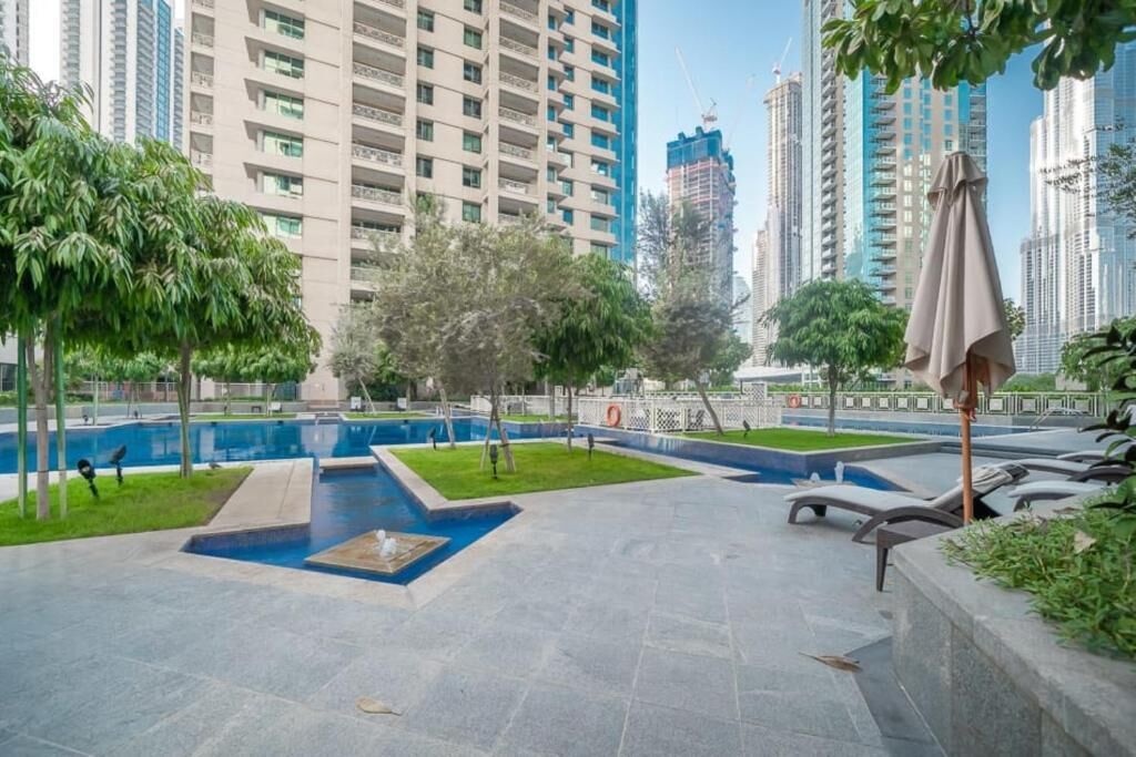 A modern outdoor pool area with a blue pool, surrounded by greenery and lounge chairs.