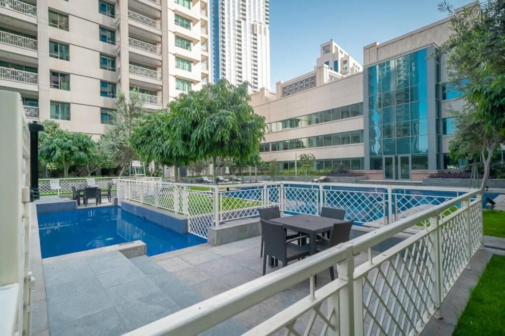 Zona de piscina en la azotea con vistas a edificios altos, mobiliario exterior y una valla blanca.