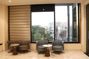 Una habitación moderna con dos sillones grises y una pequeña mesa redonda, ventanas amplias con vistas a la ciudad y una pared a rayas.