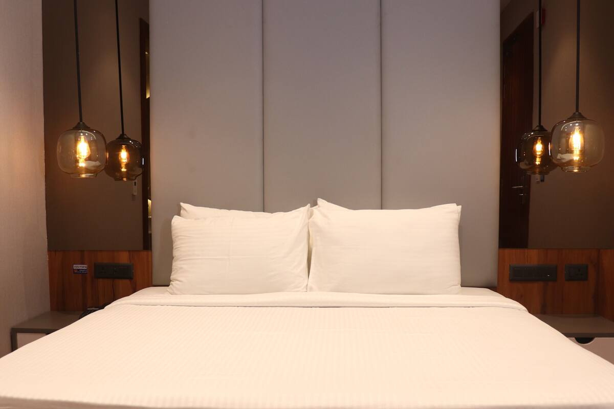 A modern hotel room with a large bed, two bedside tables, and pendant lighting.