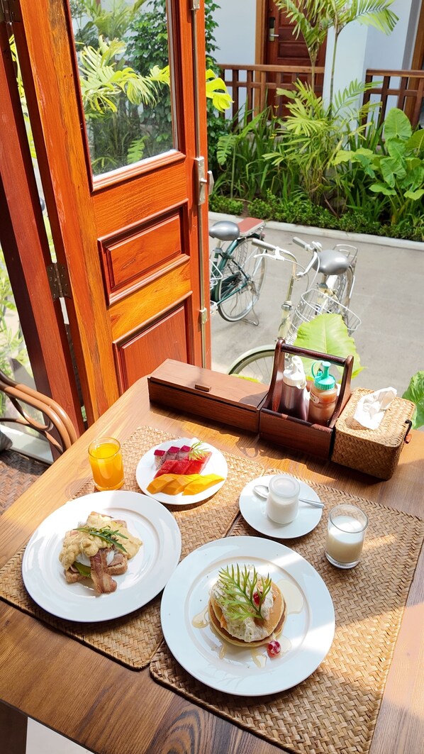 A wooden table with breakfast plates, a beverage, and a wicker basket with a bottle and a cup.