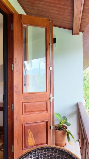A wooden door with a glass panel, a potted plant, and a metal railing on a porch.