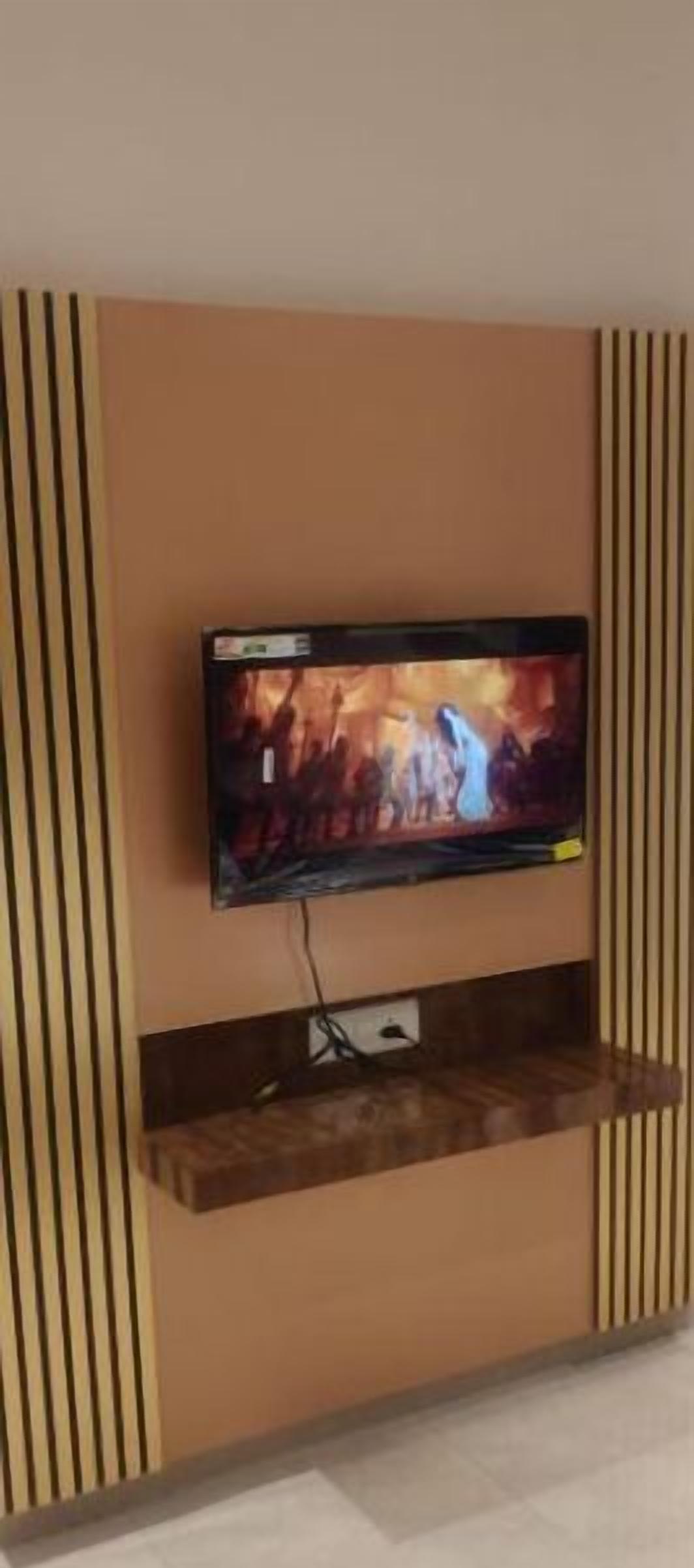 A flat-screen TV mounted on a wall with a wooden shelf below it.