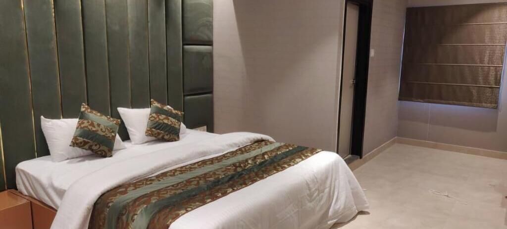 A hotel room with a bed, a headboard, and a window with blinds.