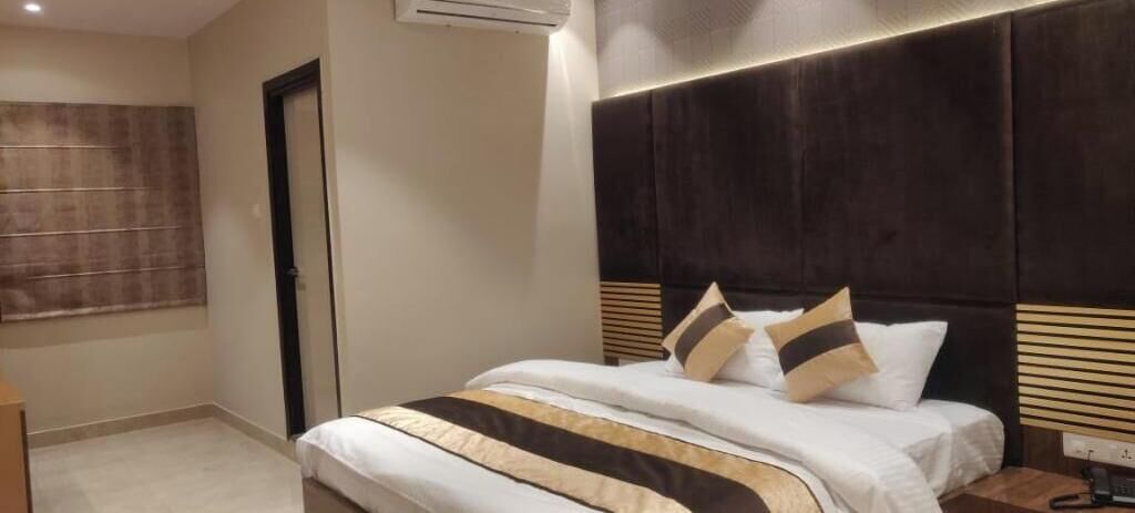 A hotel room with a large bed, a dark headboard, and a window with blinds.