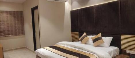 A hotel room with a large bed, a dark headboard, and a window with blinds.