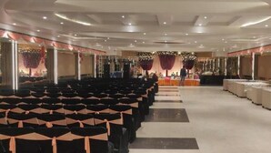 A banquet hall with rows of chairs, a stage with a table, and a seating area with sofas. - Hotel Maya Crystal (Kanpur)