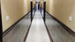 A long, narrow hallway with beige walls and a light-colored floor, leading to a door at the end. - Hotel Maya Crystal (Kanpur)