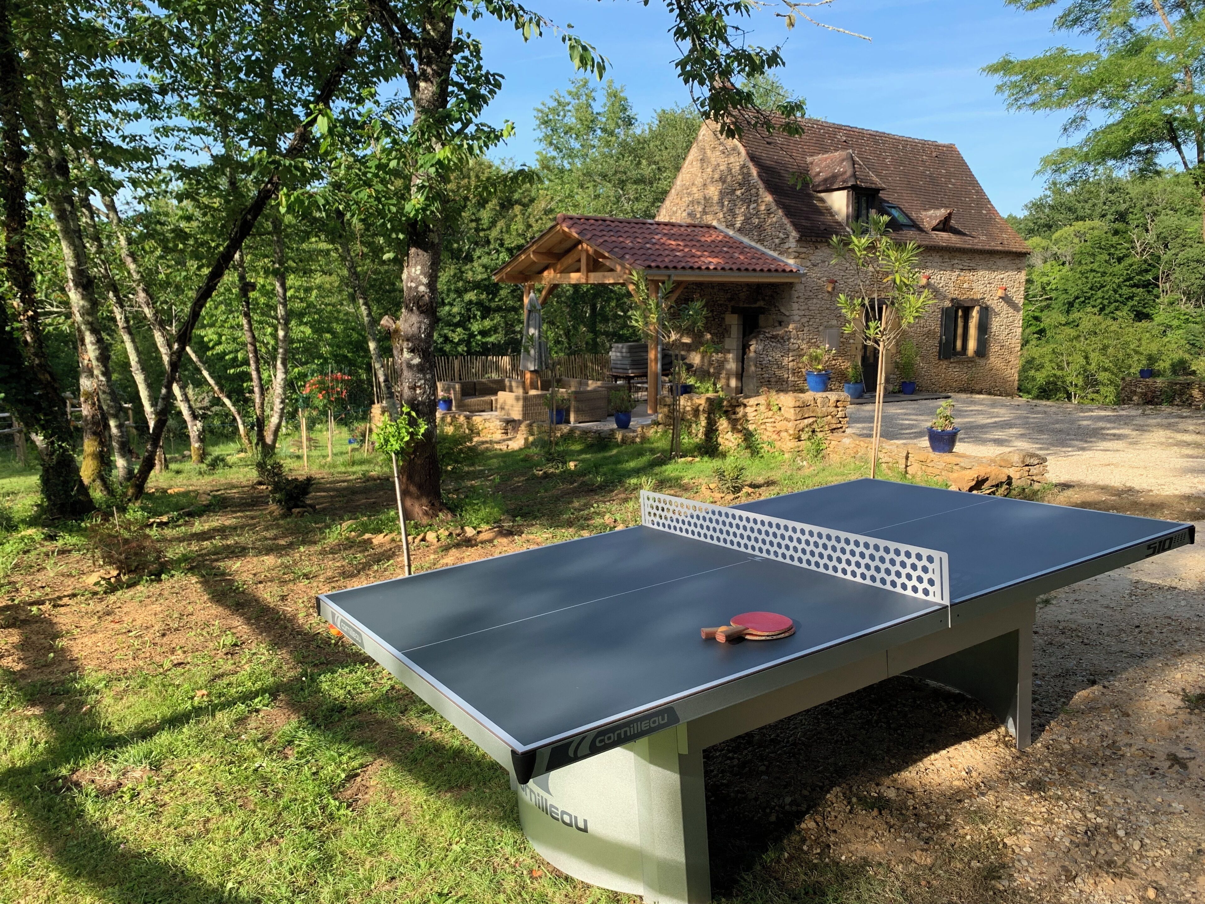 Una mesa de ping pong al aire libre con una casa de piedra al fondo.