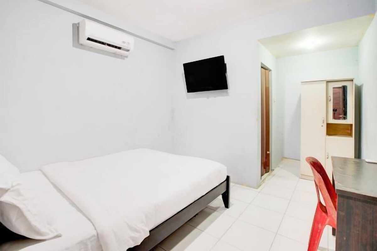 A bedroom with a bed, a TV mounted on the wall, a wardrobe, and a desk with a chair.