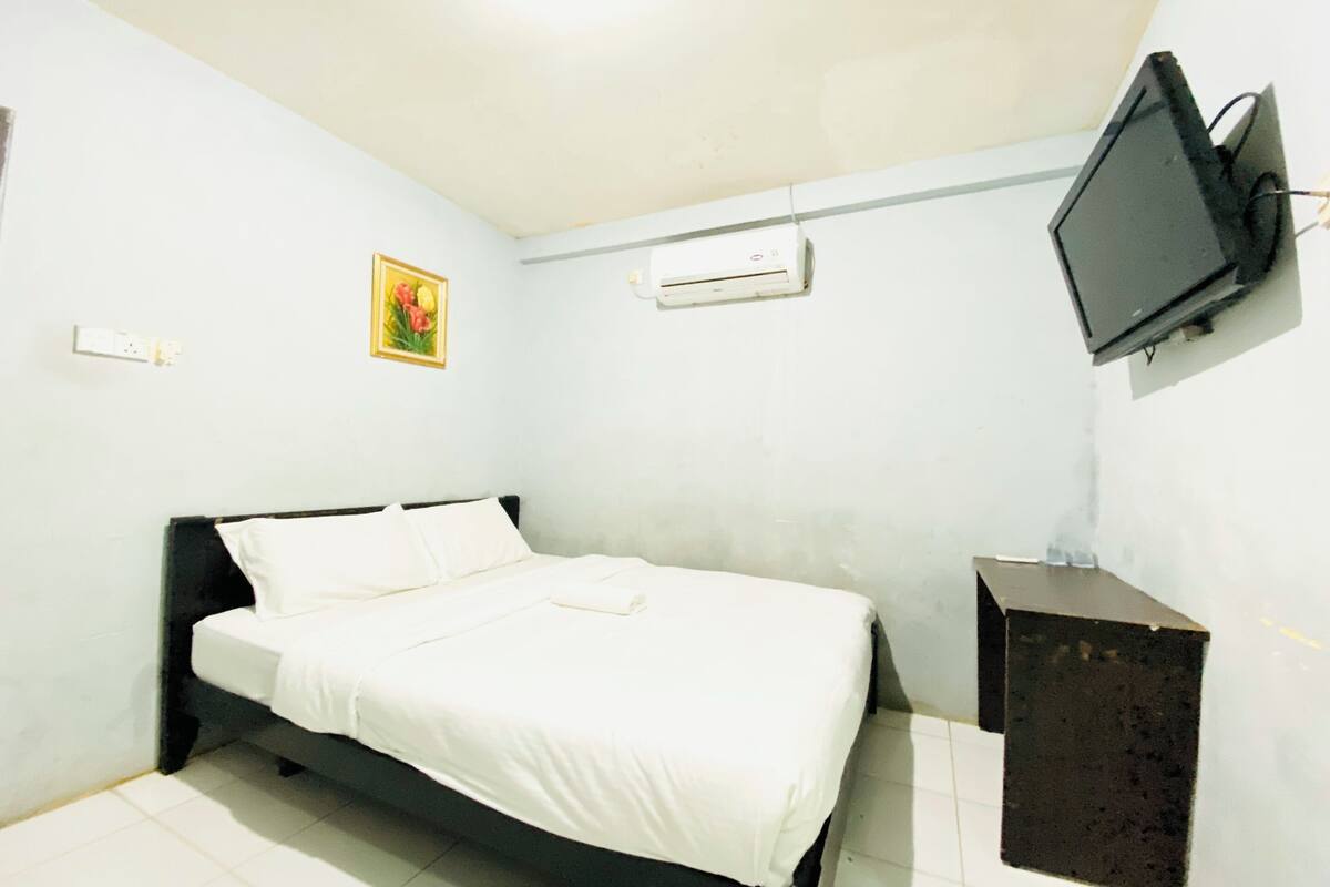 Una habitación pequeña y sencilla con una cama, un televisor montado en la pared y un equipo de aire acondicionado.