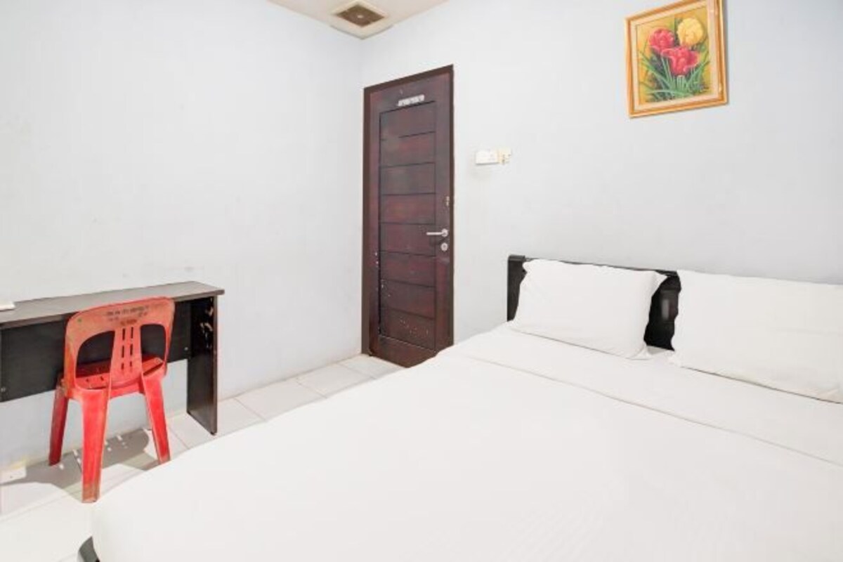 Un dormitorio con cama, un escritorio con silla, una puerta y un cuadro colgado en la pared.