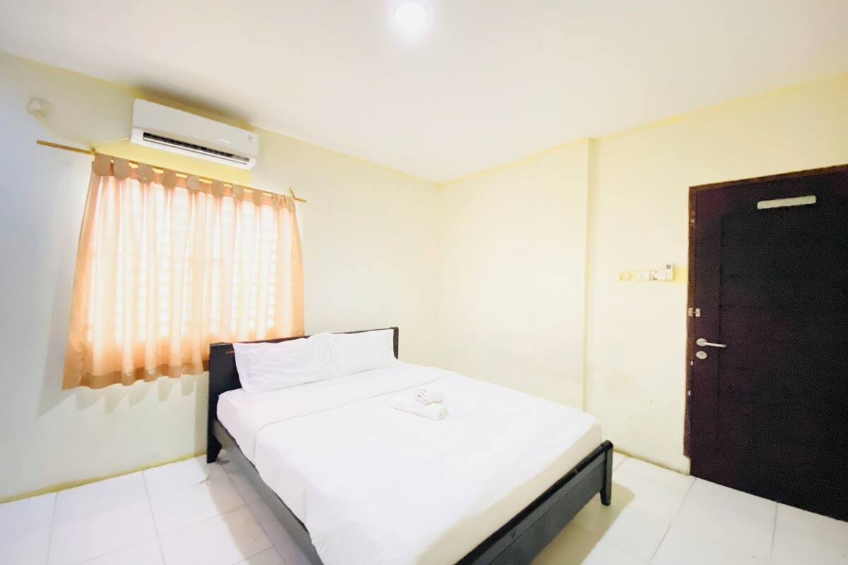 Una habitación de hotel limpia y bien iluminada, con cama, equipo de aire acondicionado y una puerta.