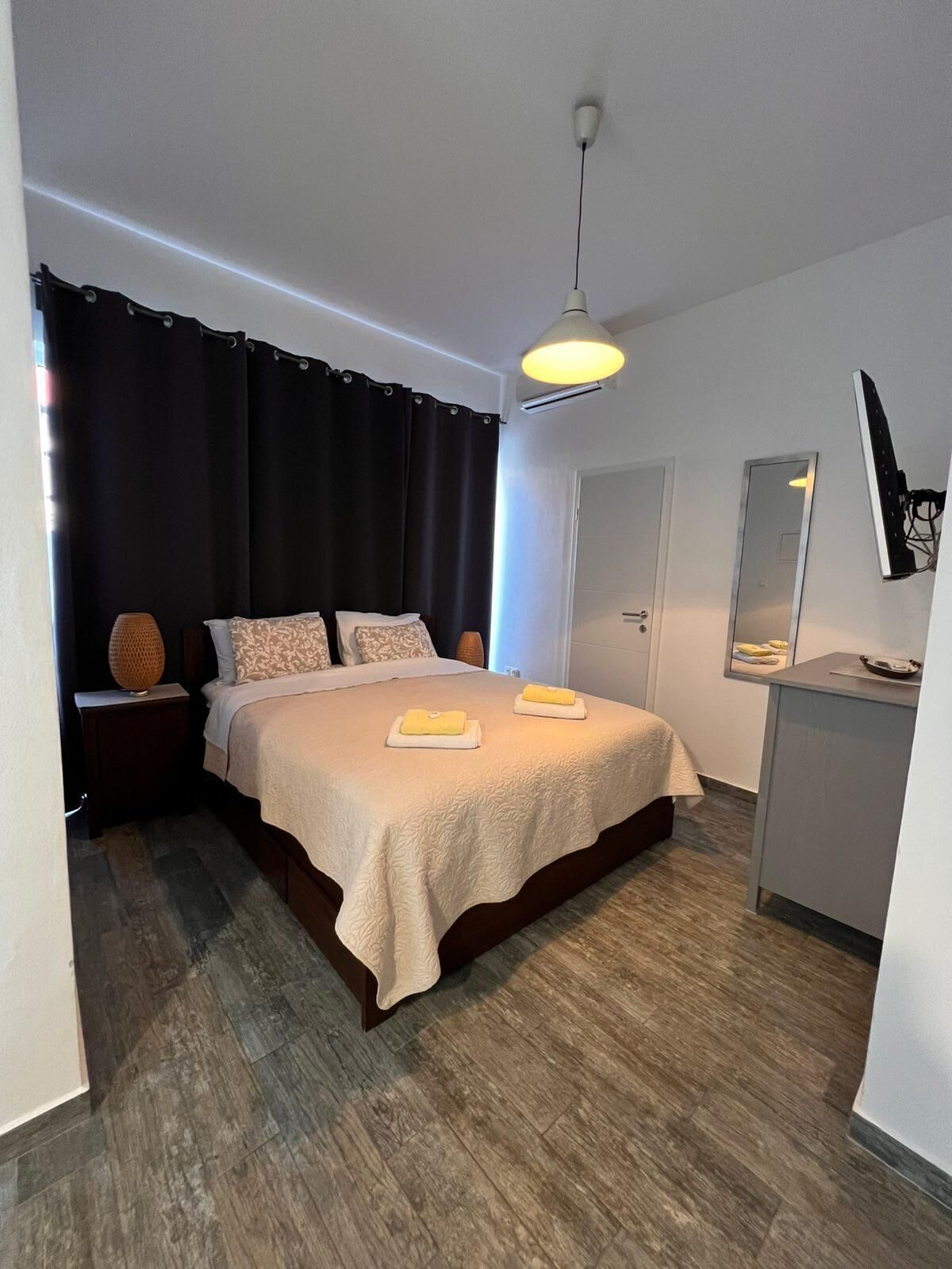 A modern bedroom with a bed, bedside lamps, a desk, and a mirror.