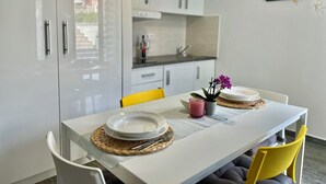 A modern kitchen with white cabinets, a built-in oven, and a dining area with a white table, yellow chairs, and a purple orchid centerpiece.