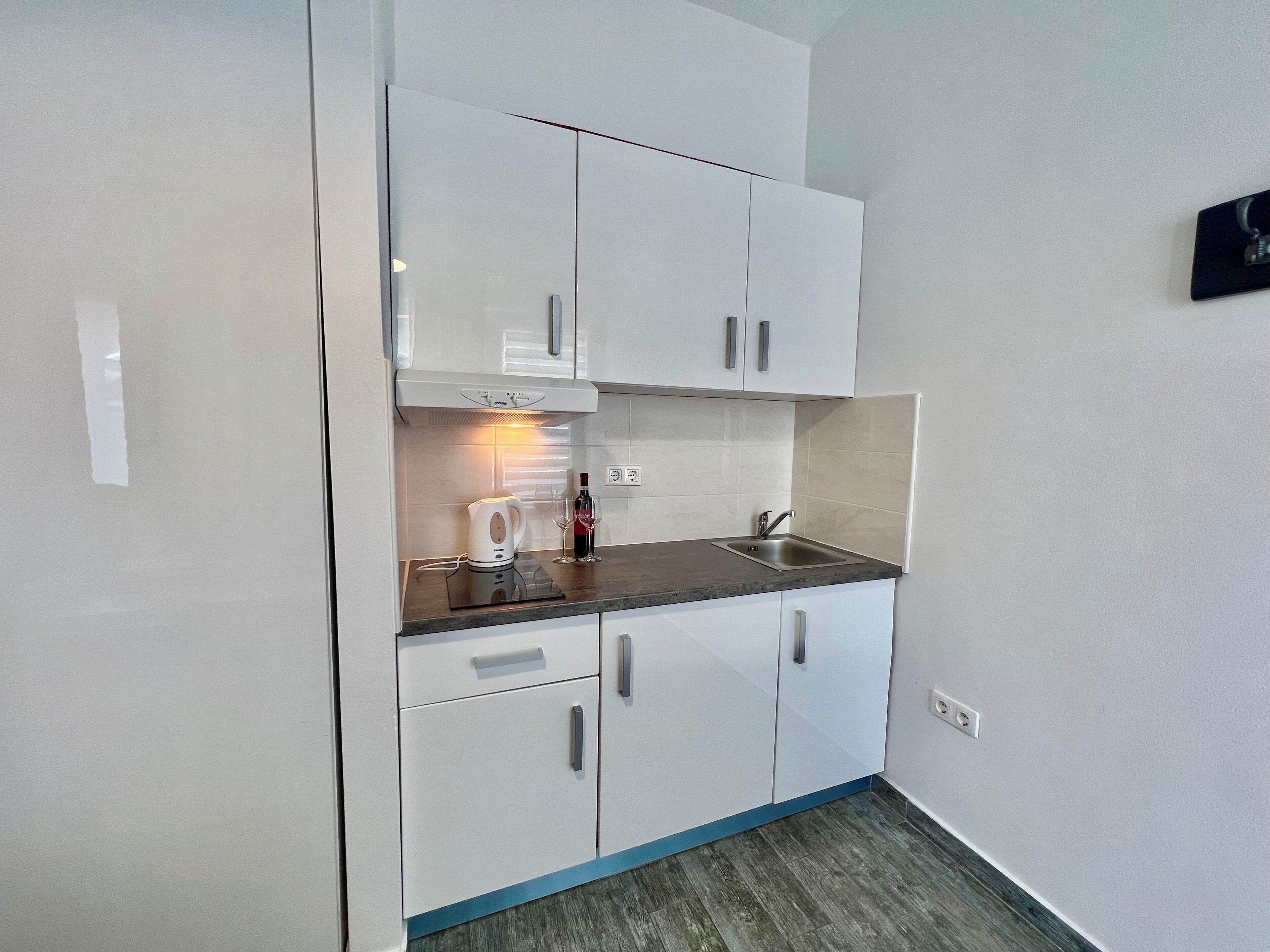 A compact kitchen with white cabinets, a built-in oven, a sink, and a countertop.