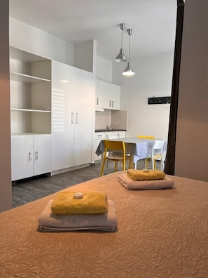 Quarto com cama, mesa e cadeiras, cozinha e luminária pendente.