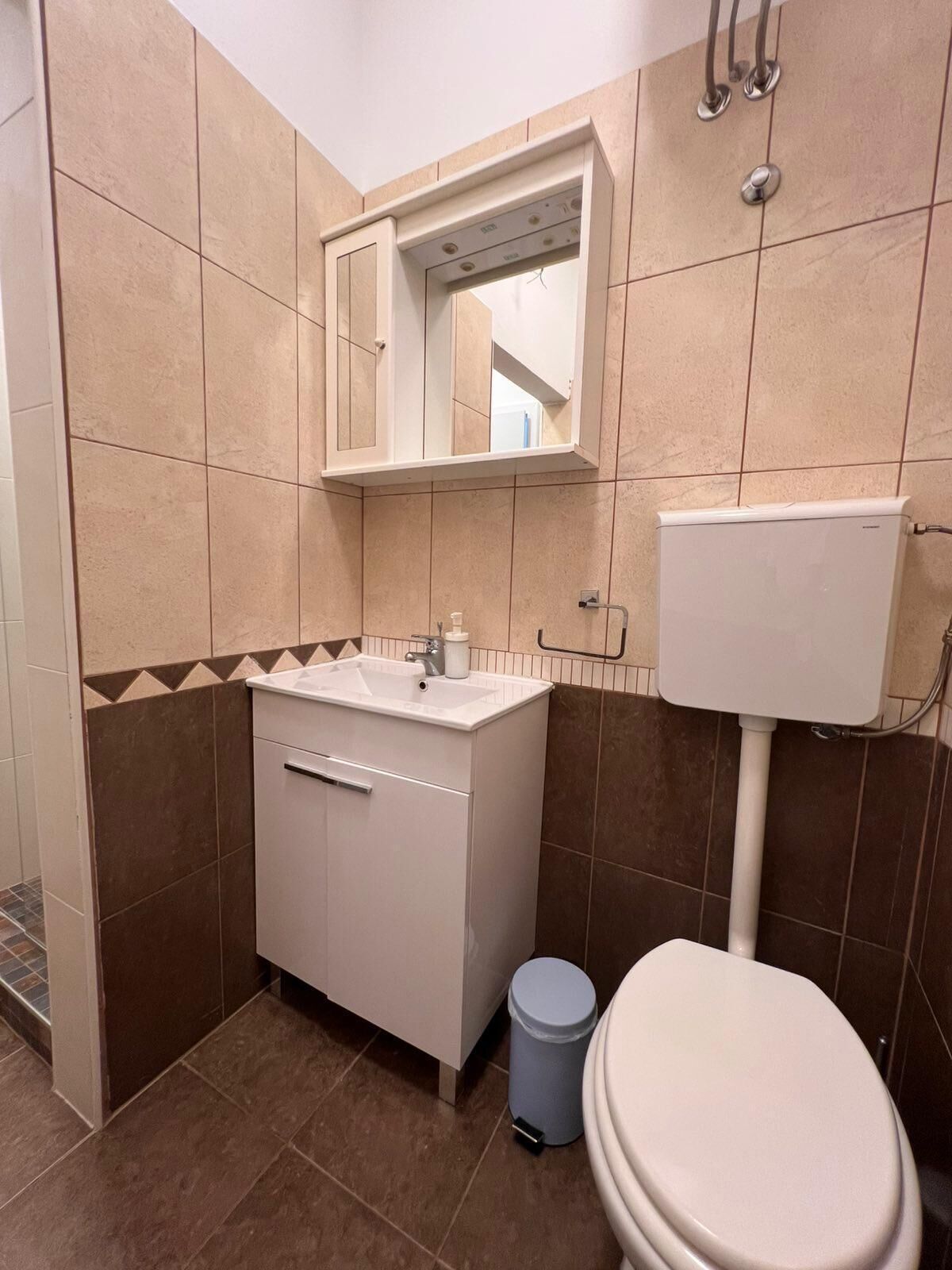 A bathroom with a toilet, sink, mirror, and tiled walls.