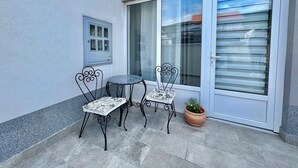 A small patio with two metal chairs and a table, a potted plant, and a sliding glass door.