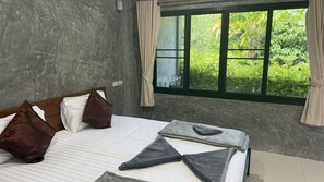 Une chambre d’hôtel avec un lit, des oreillers, une fenêtre avec des rideaux et une vue sur la verdure environnante.
