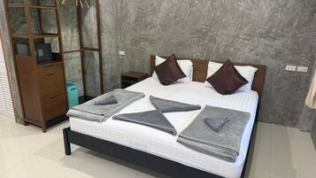 A neatly made bed with pillows and folded towels, a wooden nightstand with a lamp, and a wall-mounted shelf with a basket.