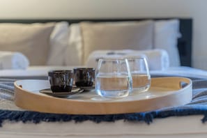 Una cama con una bandeja de madera que sostiene dos vasos de agua y dos tazas, sobre una colcha azul y blanca a rayas.