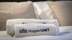 Two white towels with "ProperUNIT" embroidered on them, placed on a bed with a headboard. - Apartament w Śródmieściu Odnowa (Wroclaw)