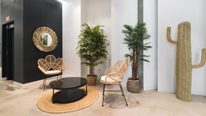 A modern interior with a black wall, a round mirror, wicker chairs, a round table, and potted plants. - Stayaday Apartments Albufera (Madrid)