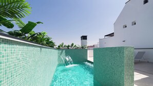 A swimming pool with a clear blue water feature, surrounded by a tiled wall and lush greenery. - Stayaday Apartments Albufera (Madrid)