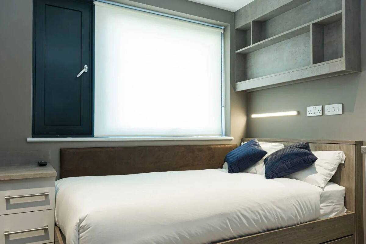 Una camera da letto con un letto, comodini, una finestra con tende, scaffalature a muro e una testiera.