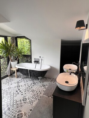 Un bagno moderno con una vasca da bagno indipendente, due lavabi, uno specchio grande e una pianta in vaso.