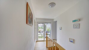 Un couloir avec un escalier en bois, une porte donnant sur un balcon et un luminaire au plafond.