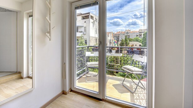 Une pièce dotée d’une porte-fenêtre coulissante donnant sur un balcon avec vue sur les bâtiments et un ciel dégagé.