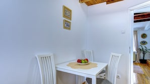 Un petit coin repas avec une table blanche, deux chaises et un saladier de fruits. Deux tableaux encadrés sont accrochés au mur.
