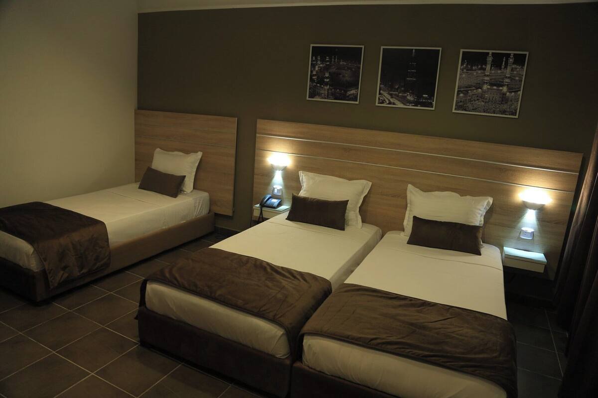 Een hotelkamer met drie eenpersoonsbedden, elk met een houten hoofdeinde en bedlampjes.