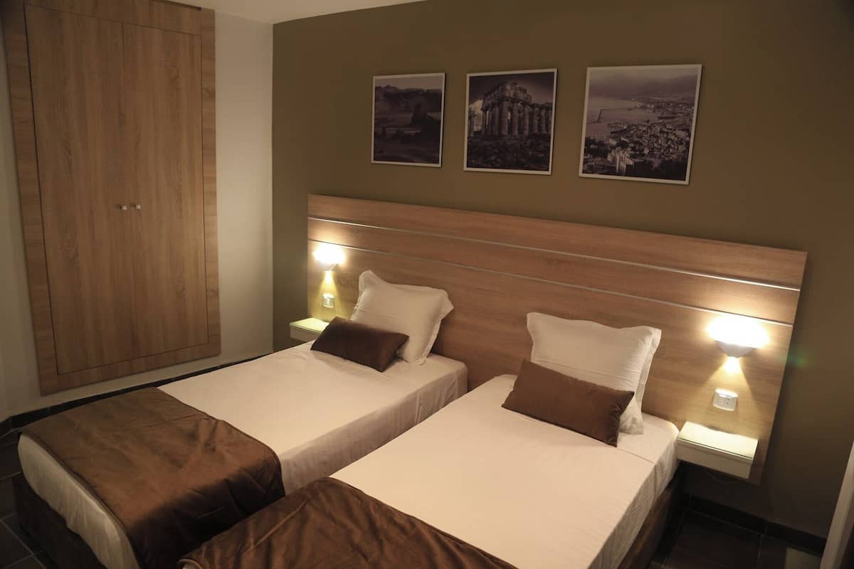 Een hotelkamer met twee bedden, een houten hoofdeinde, nachtkastjes met lampen en drie ingelijste foto's aan de muur.